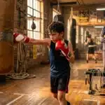 Enfant boxe au sac avec entraîneur observant en arrière-plan