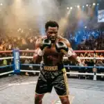 Boxeur avec gants noirs et or dans un ring devant une foule